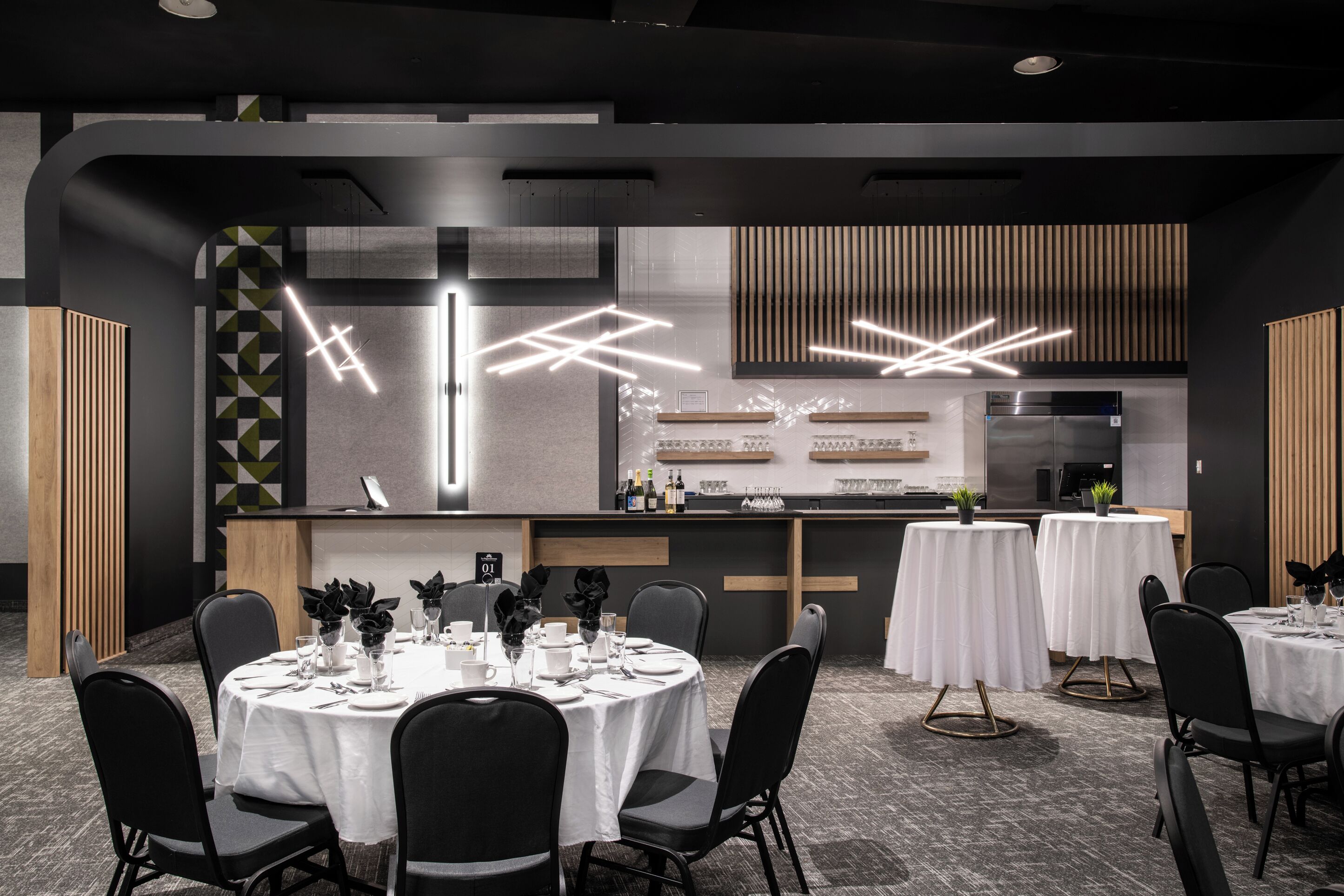 Un comedor moderno con mesas redondas, sillas negras y una zona de bar central, con una cocina al fondo.
