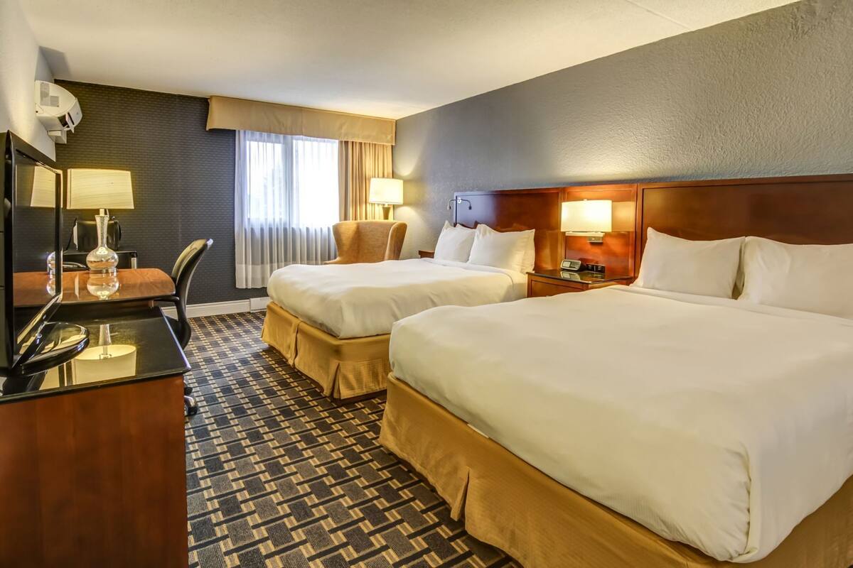 Ett hotellrum med två sängar, ett skrivbord med en lampa, en stol, ett sängbord med en lampa och en mönstrad matta.