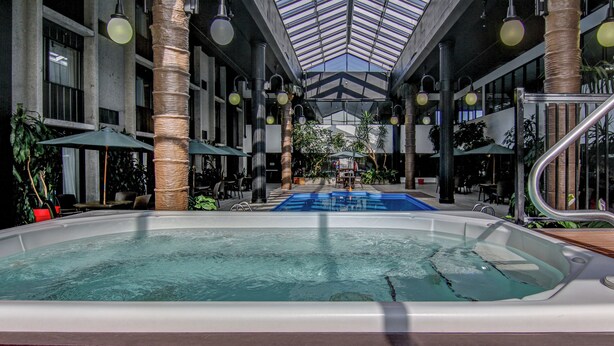 Una piscina interior con techo de vidrio, rodeada de columnas y zonas de descanso.