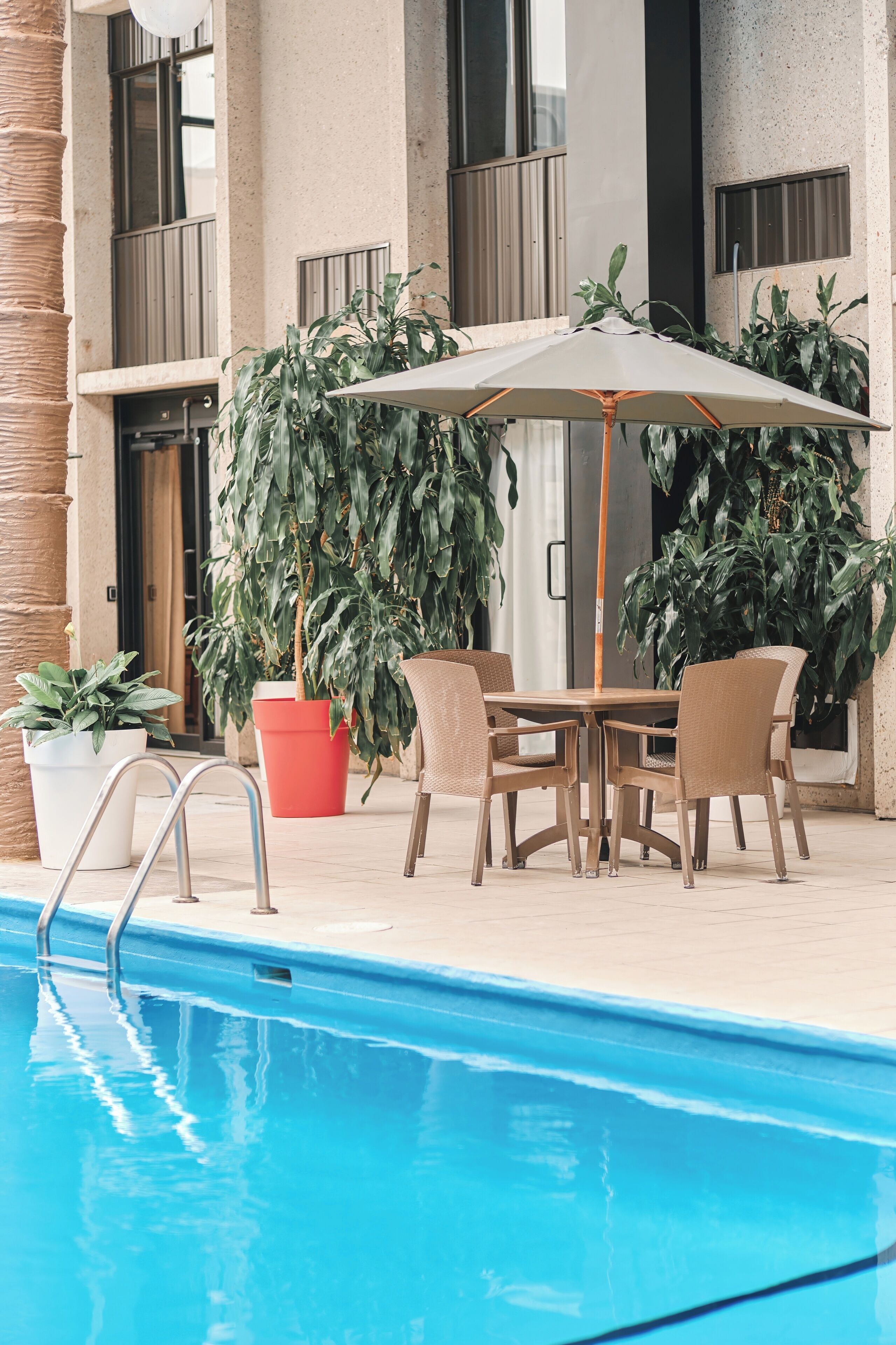 A poolside area with a table and chairs, surrounded by potted plants and a large umbrella.