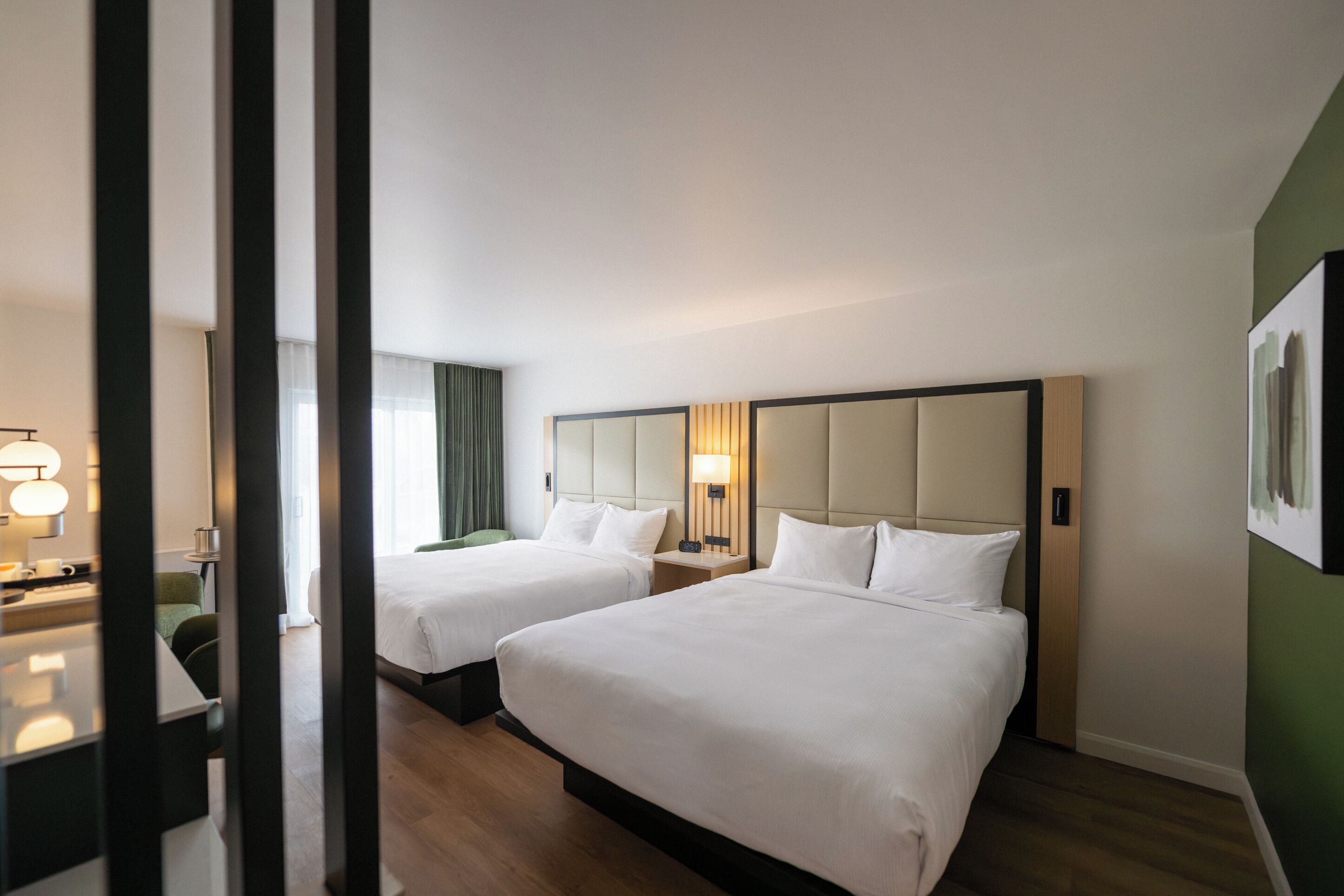 A hotel room with two beds, a bedside table, a lamp, and a window with curtains.