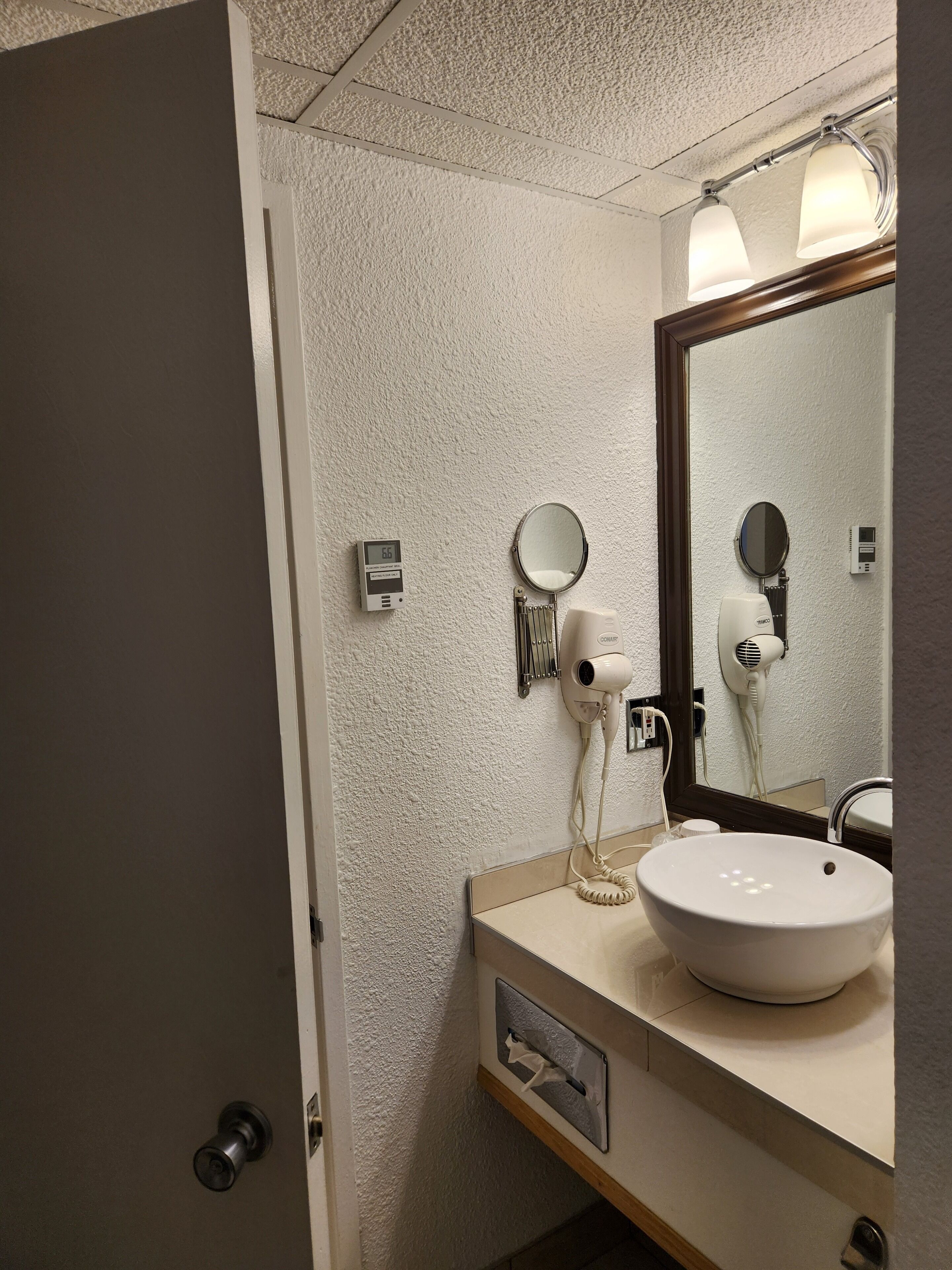 A bathroom with a white sink, a mirror, a hairdryer, and a digital clock.