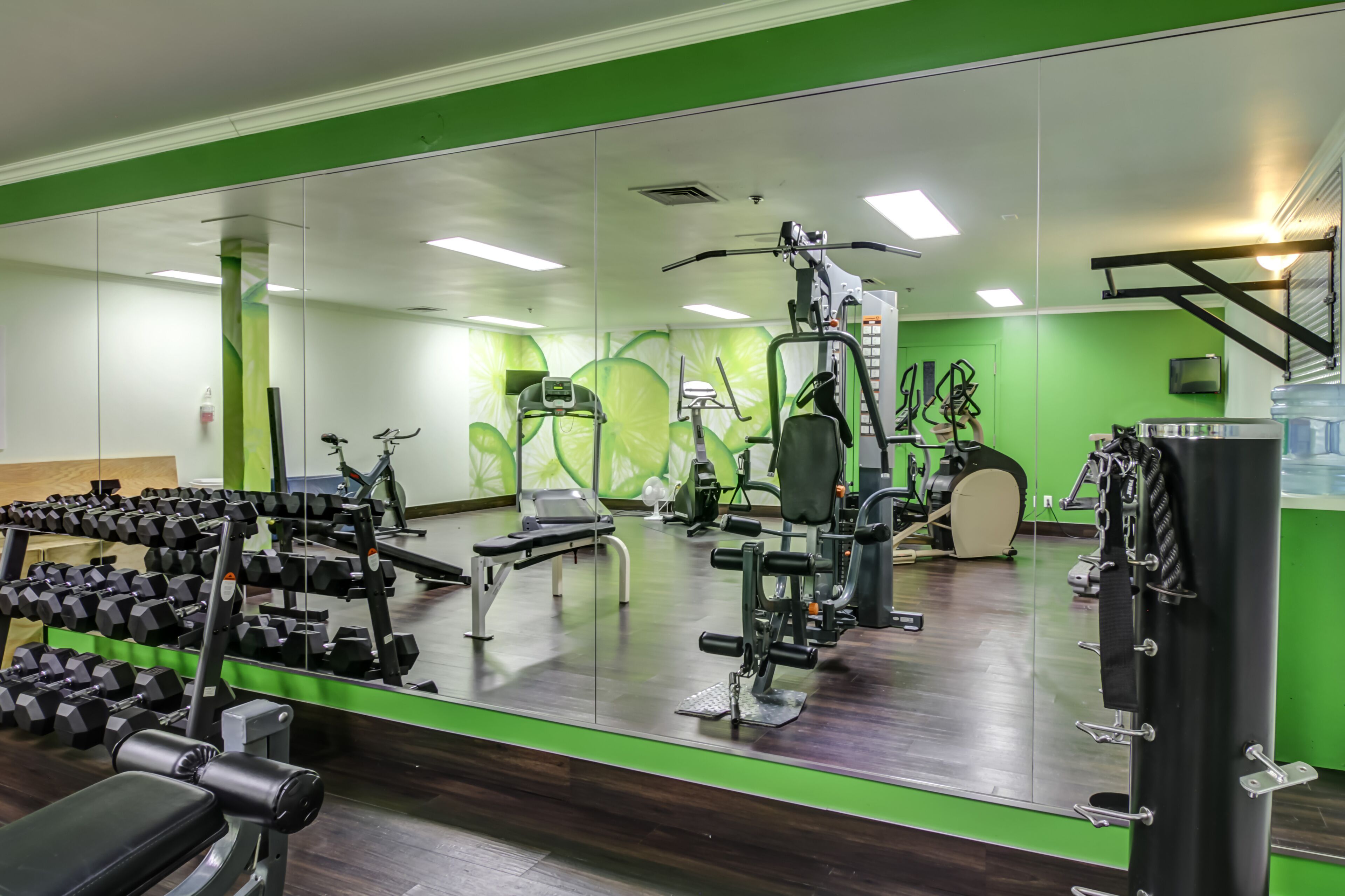 Uma academia com paredes espelhadas, equipamentos de ginástica e uma parede com detalhes em verde.