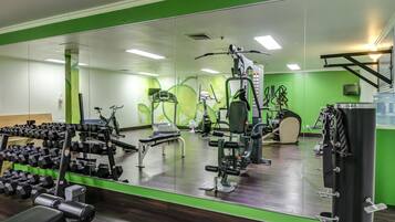Uma academia com paredes espelhadas, equipamentos de ginástica e uma parede com detalhes em verde.