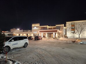 A building with a stone facade and a lit entrance. - La Saguenéenne - Hôtel et Centre de Congrès (Saguenay)