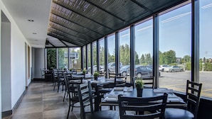 Un comedor interior con mesas y sillas, ventanas amplias y un estacionamiento visible al exterior.