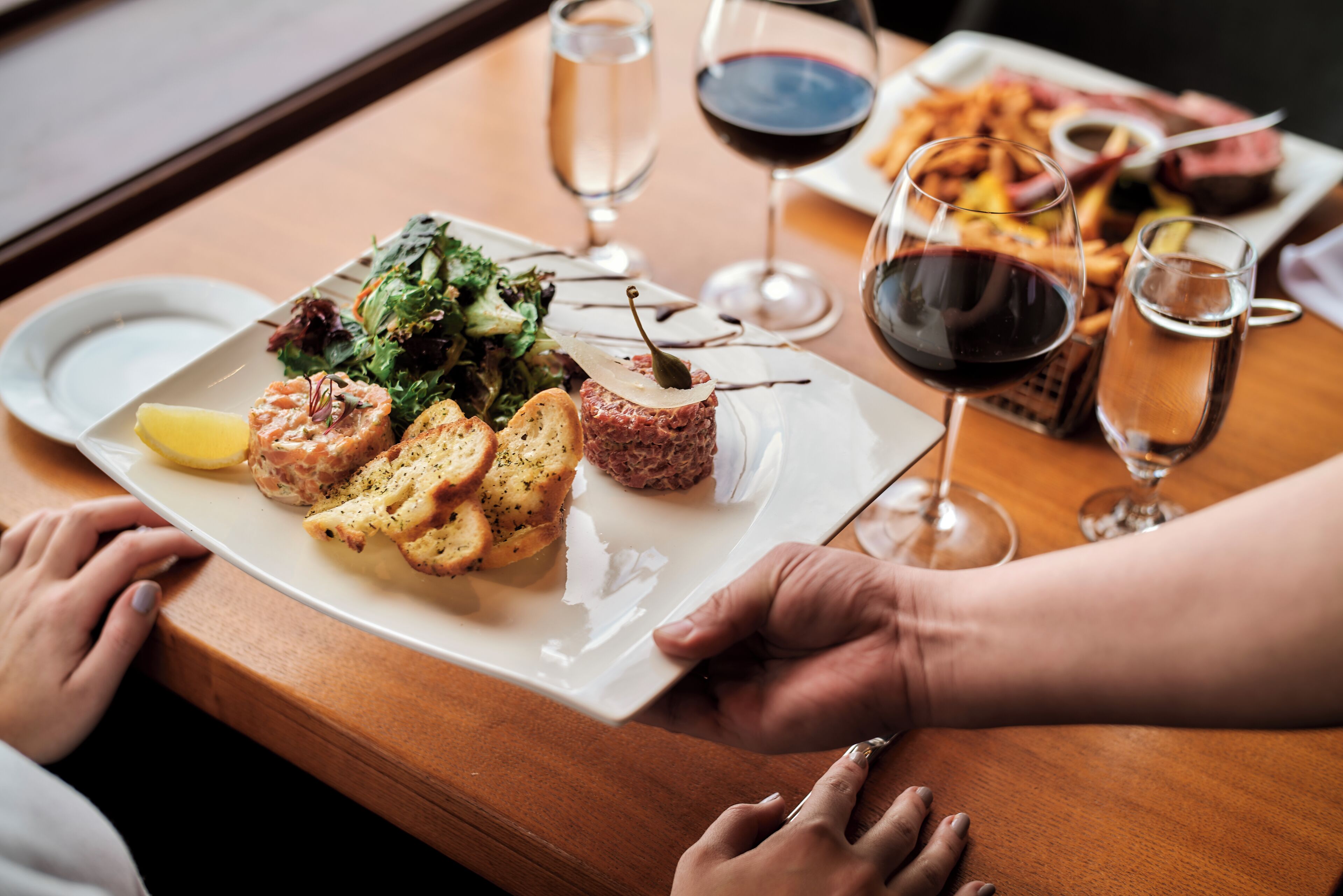 Una mesa con un plato de comida, copas de vino y una persona sosteniendo un plato.