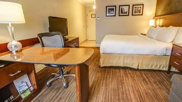 Habitación de hotel con cama, escritorio con lámpara, silla, televisor y piso alfombrado.