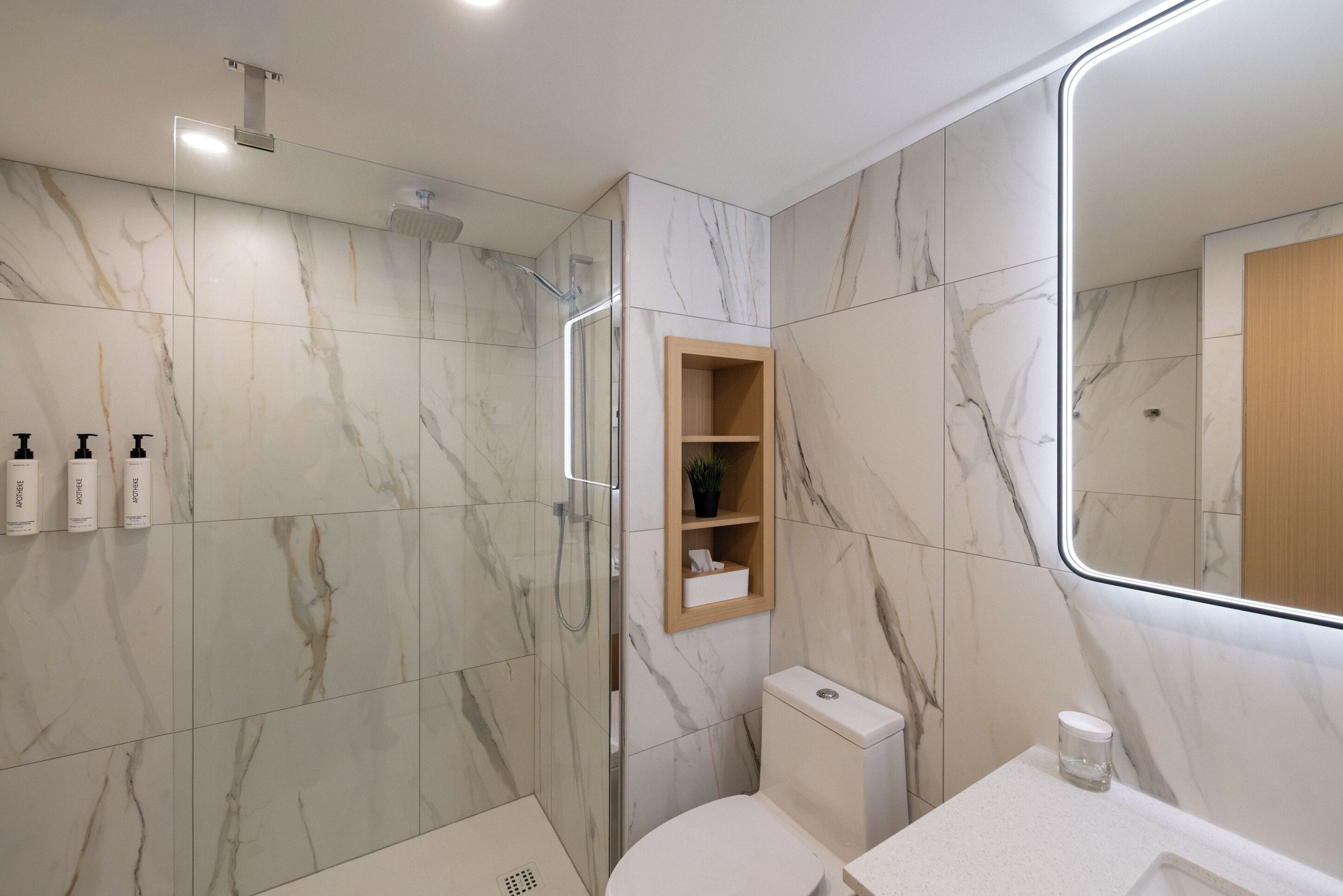 Un baño moderno con cabina de ducha de vidrio, inodoro y tocador con espejo.