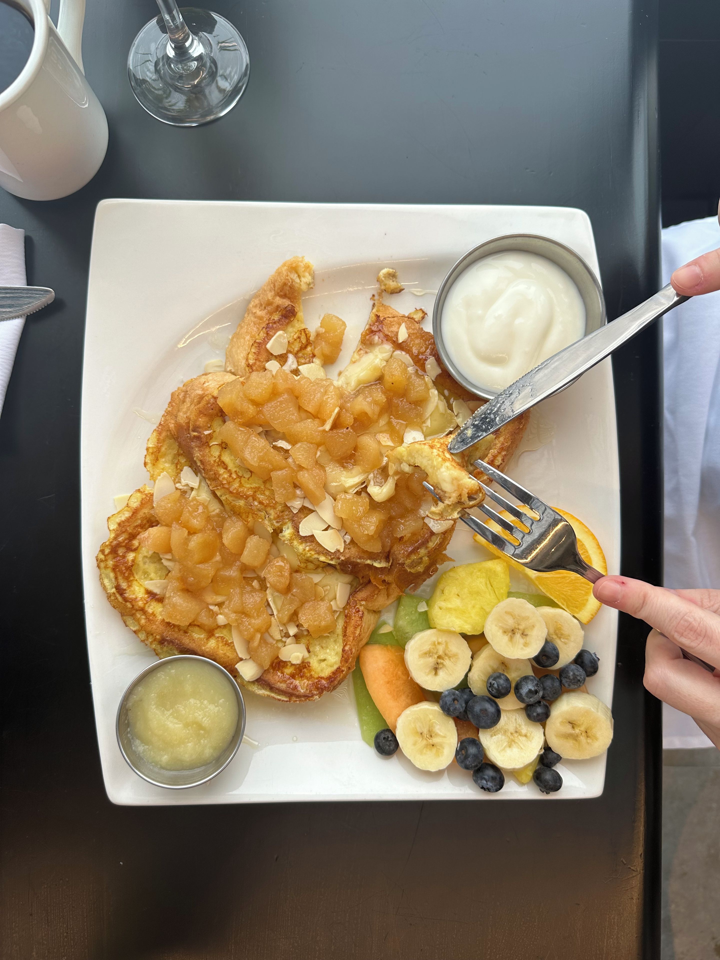 Une assiette contenant un petit-déjeuner composé de crêpes garnies de fruits et d’un petit bol de yaourt.