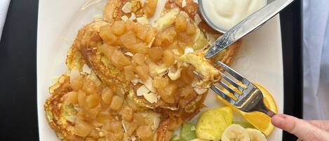 Une assiette contenant un petit-déjeuner composé de crêpes garnies de fruits et d’un petit bol de yaourt.