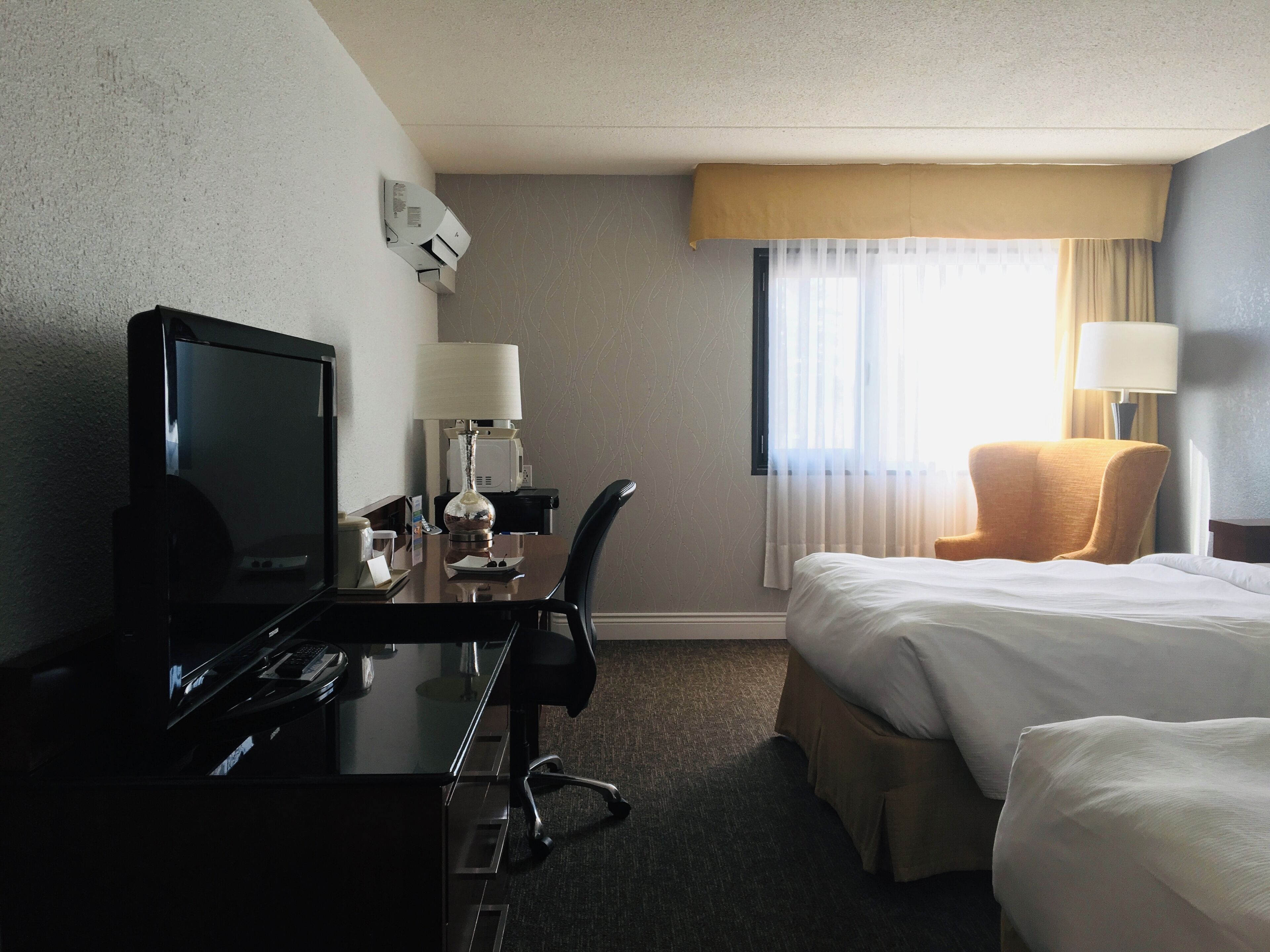 A hotel room with a desk, a bed, a chair, and a television.