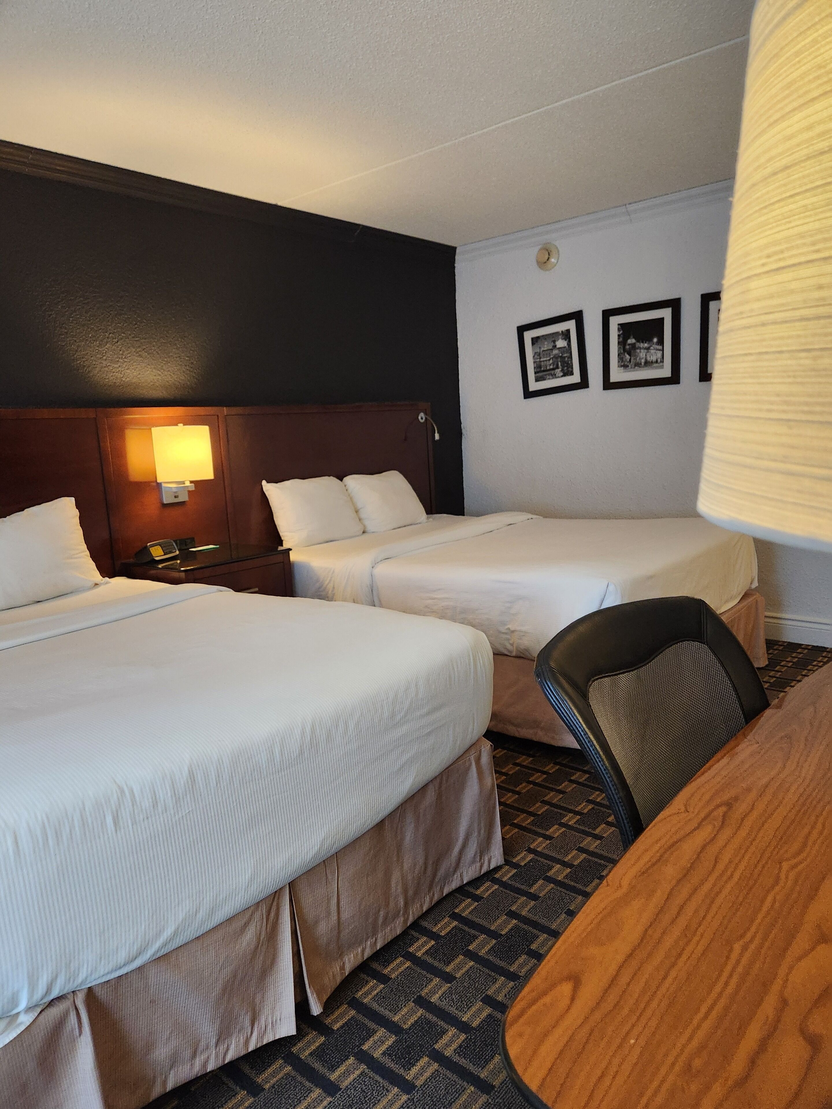 A hotel room with two beds, a desk, and a chair. There are framed pictures on the wall.