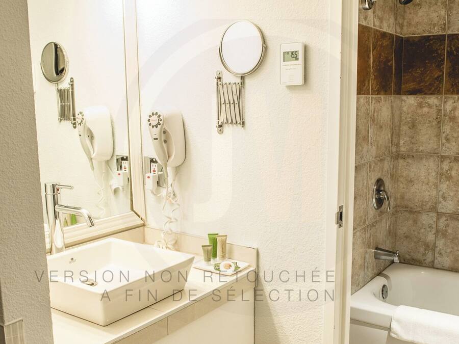 Une salle de bain avec un lavabo blanc, un miroir, un sèche-cheveux et une douche.