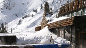 A pool area with clear water, surrounded by snow-covered mountains and a wooden building with a stone chimney. - Alta Peruvian Lodge (Sandy)