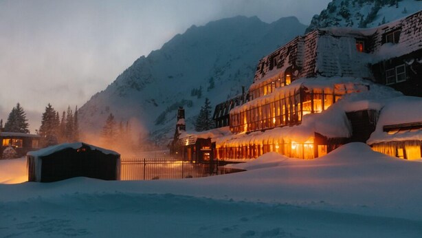 A snow-covered mountain lodge with a warm-lit facade and a snow-covered roof. - Alta Peruvian Lodge (Sandy)