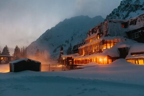 A snow-covered mountain lodge with a warm-lit facade and a snow-covered roof. - Alta Peruvian Lodge (Sandy)