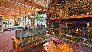 A cozy lounge area with a stone fireplace, wooden furniture, and a view of the outdoors. - Alta Peruvian Lodge (Sandy)