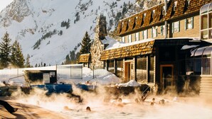 A spa area with hot tubs in front of a wooden building with stone accents, surrounded by snow-covered mountains. - Alta Peruvian Lodge (Sandy)