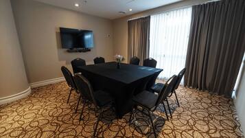 A conference room with a large table, six chairs, a flat-screen TV mounted on the wall, and a patterned carpet.