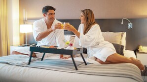 A couple sitting on a bed in a hotel room, holding glasses of orange juice. - Amérian Buenos Aires (Buenos Aires)