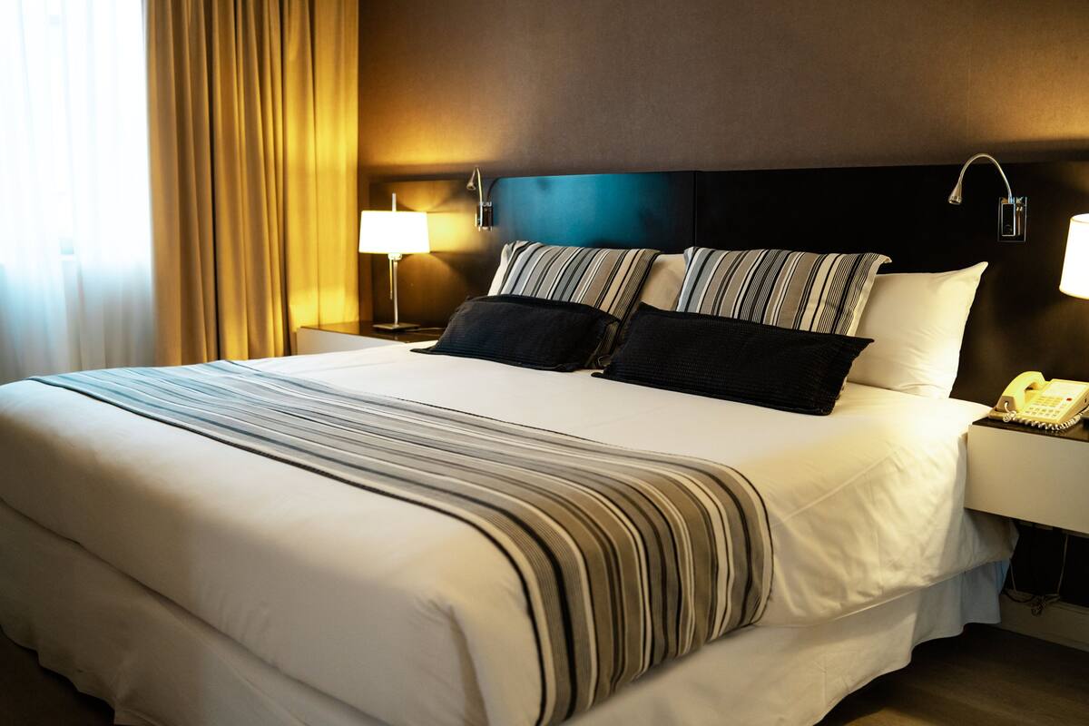 Ein Hotelzimmer mit einem großen Bett, einem Nachttischtelefon und einer Lampe auf dem Nachttisch.