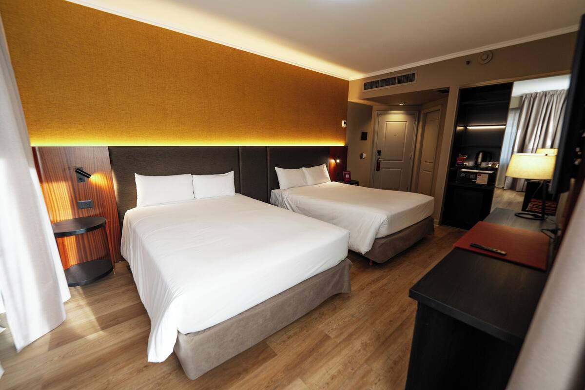 Ein Hotelzimmer mit zwei Betten, einem Schreibtisch, einem Spiegel und einem Kleiderschrank.