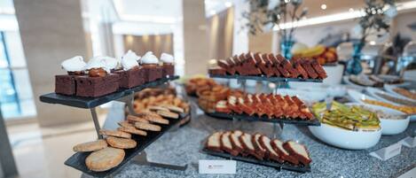 Un bufé con diversos alimentos, entre ellos brownies, galletas y sándwiches.