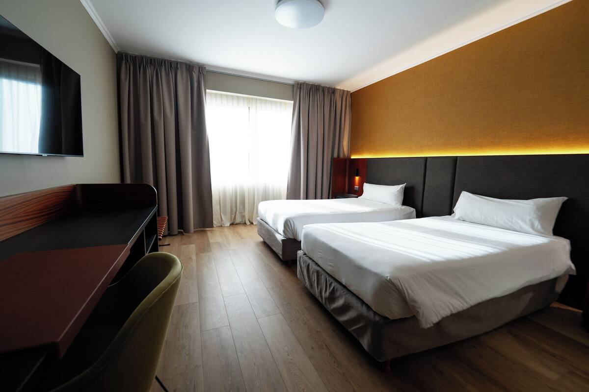 Ein Hotelzimmer mit zwei Betten, einem Schreibtisch und einem Fernseher.