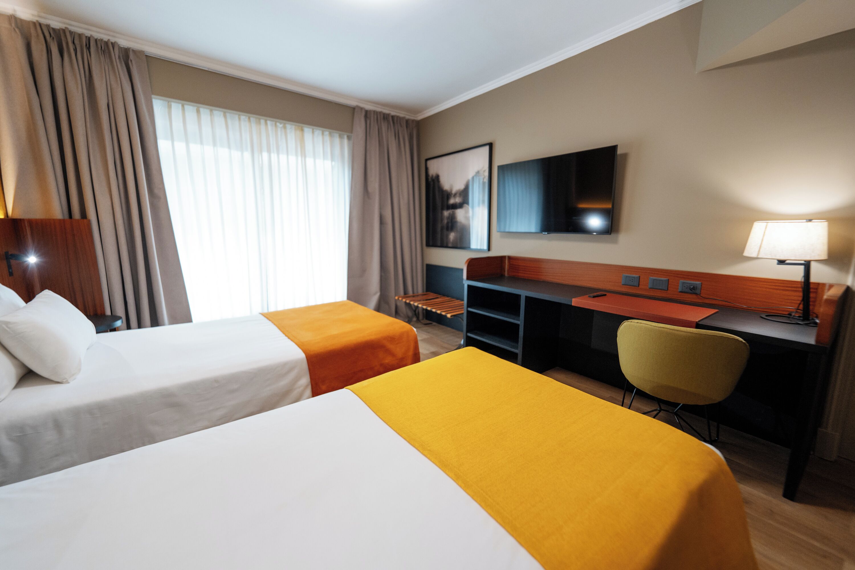 Una habitación de hotel con dos camas, un escritorio, una silla, un televisor y una lámpara.
