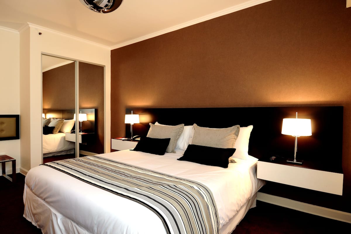Una habitació d'hotel amb un llit gran, taules de nit, un mirall i una tauleta de nit amb una làmpada.