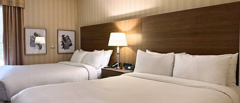 A hotel room with two beds, a nightstand with a lamp, and two framed pictures on the wall.