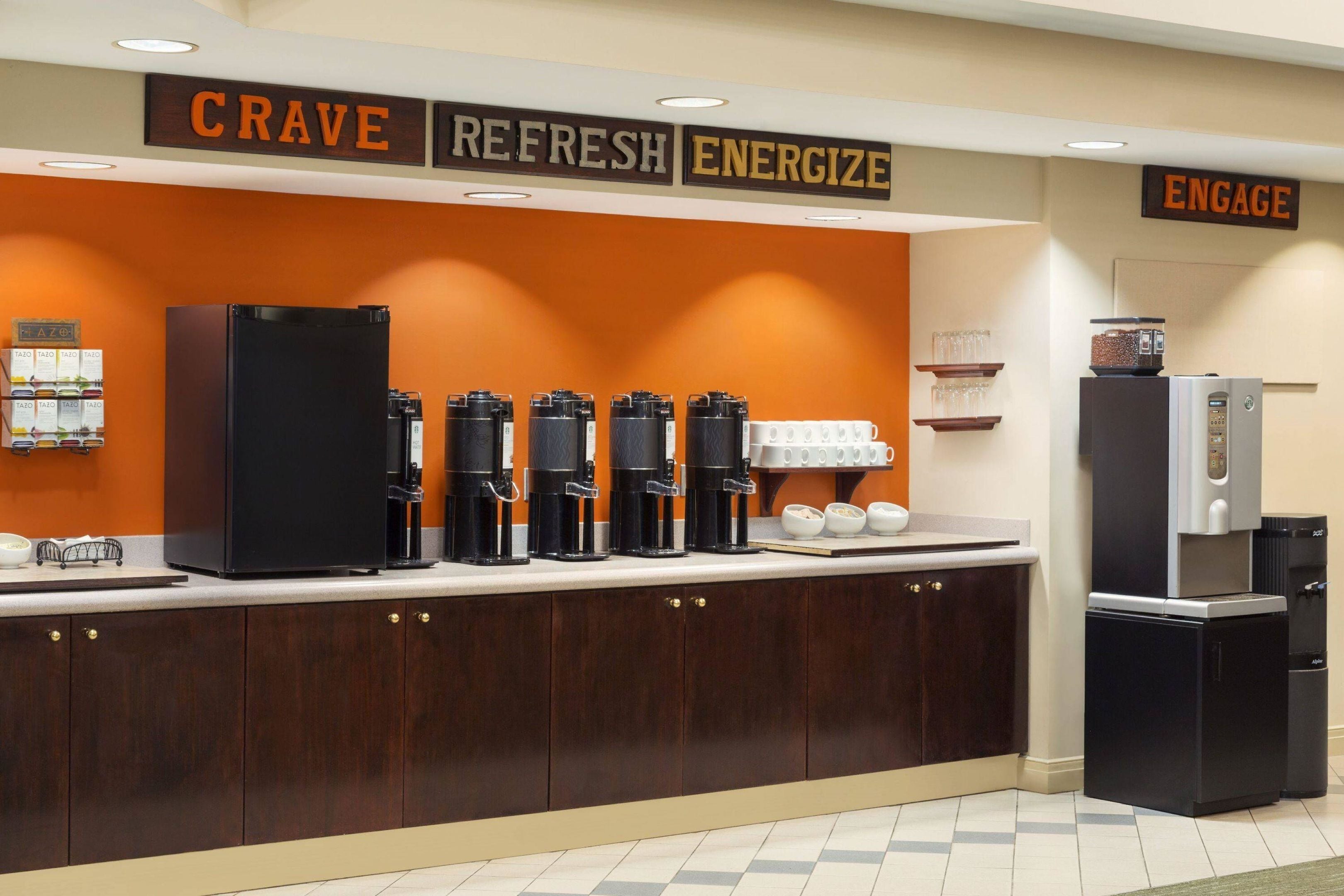 A kitchen area with a coffee station, a refrigerator, and a sign with motivational words.