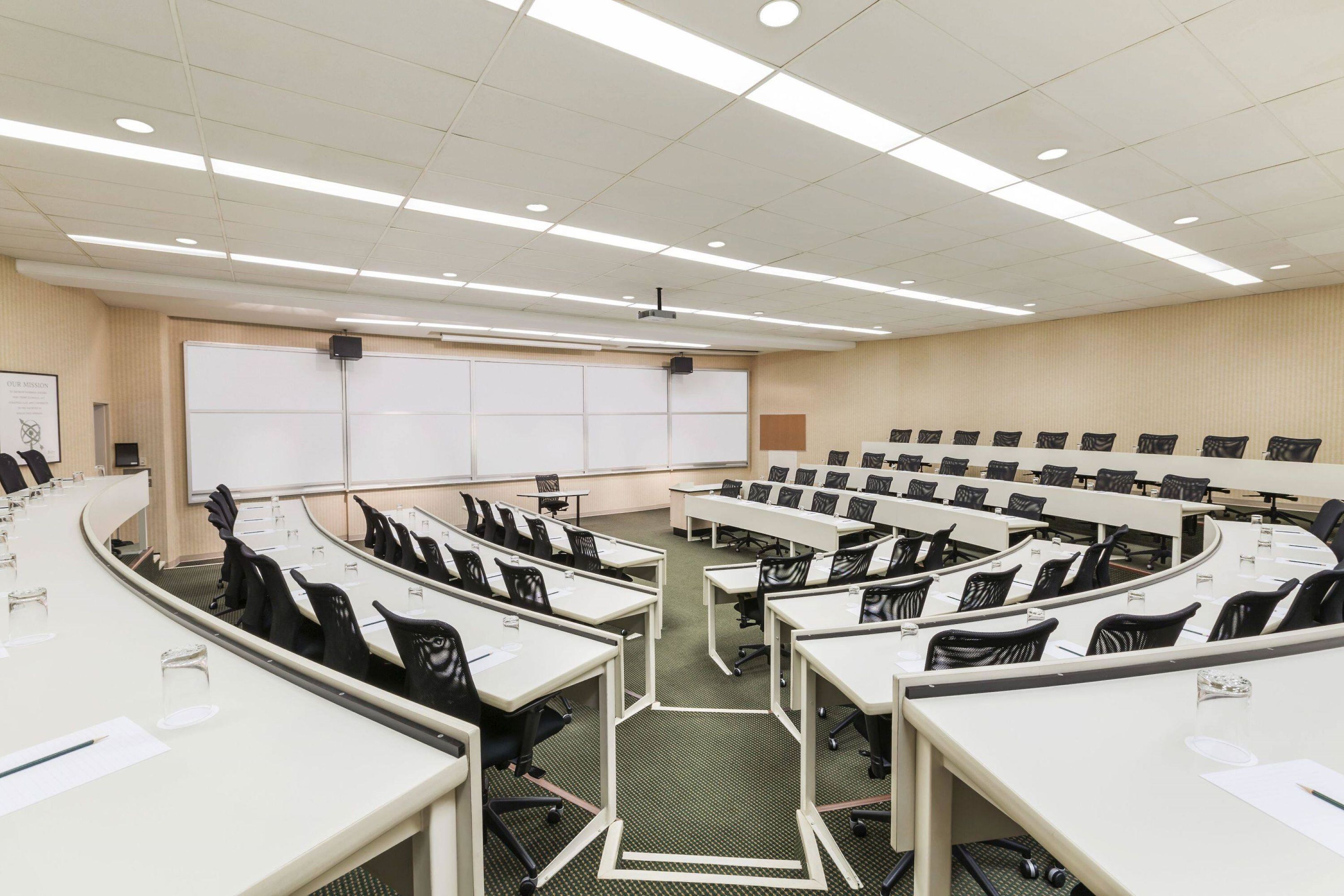 Una sala de conferencias con varias mesas y sillas, una pizarra y un proyector.