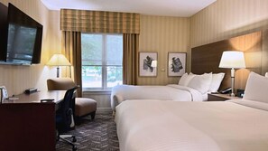 A hotel room with two beds, a desk, a chair, a TV, and two framed pictures on the wall.