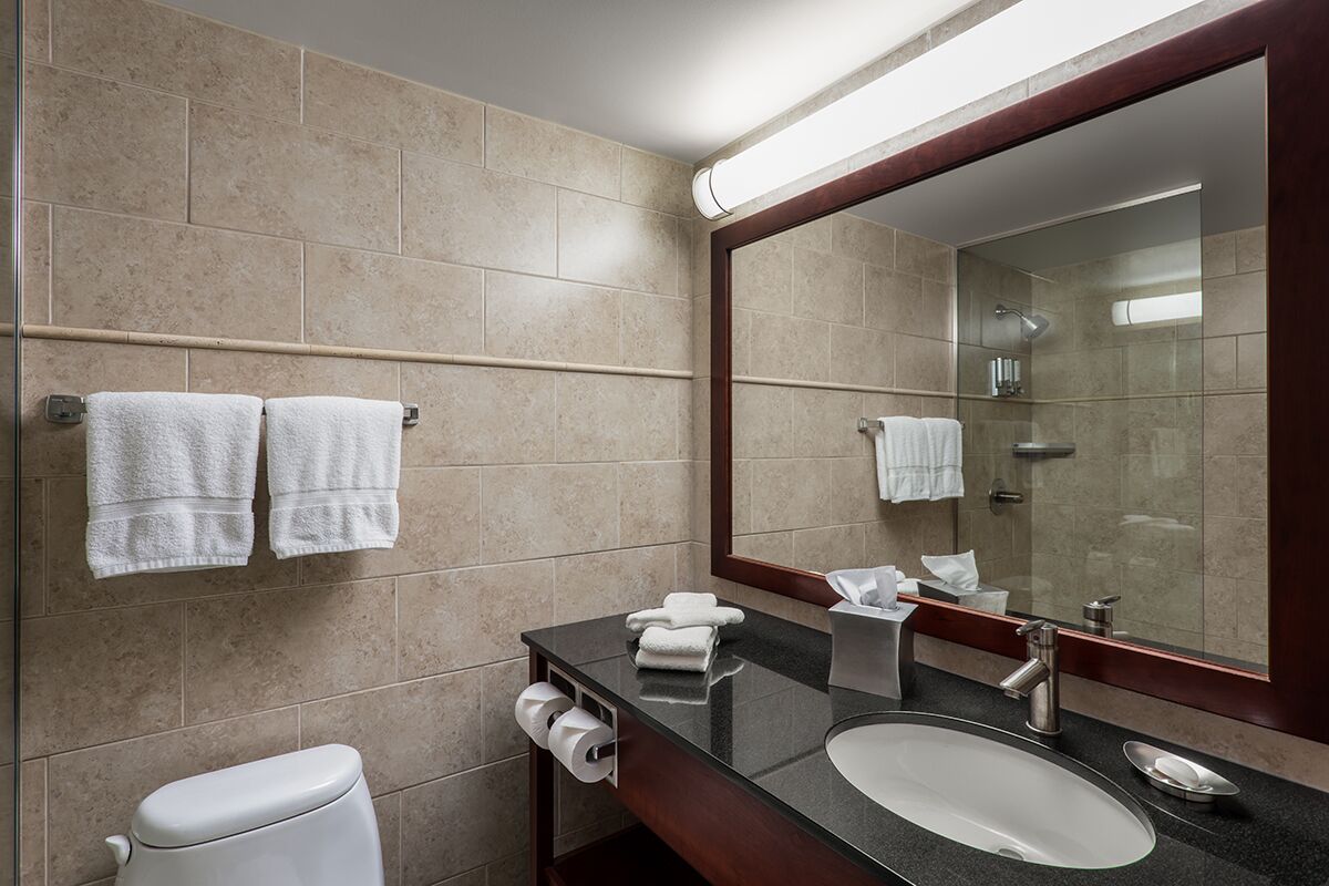 A modern bathroom with beige tiles, a black countertop, a white sink, a large mirror, and two towels on a towel rack.