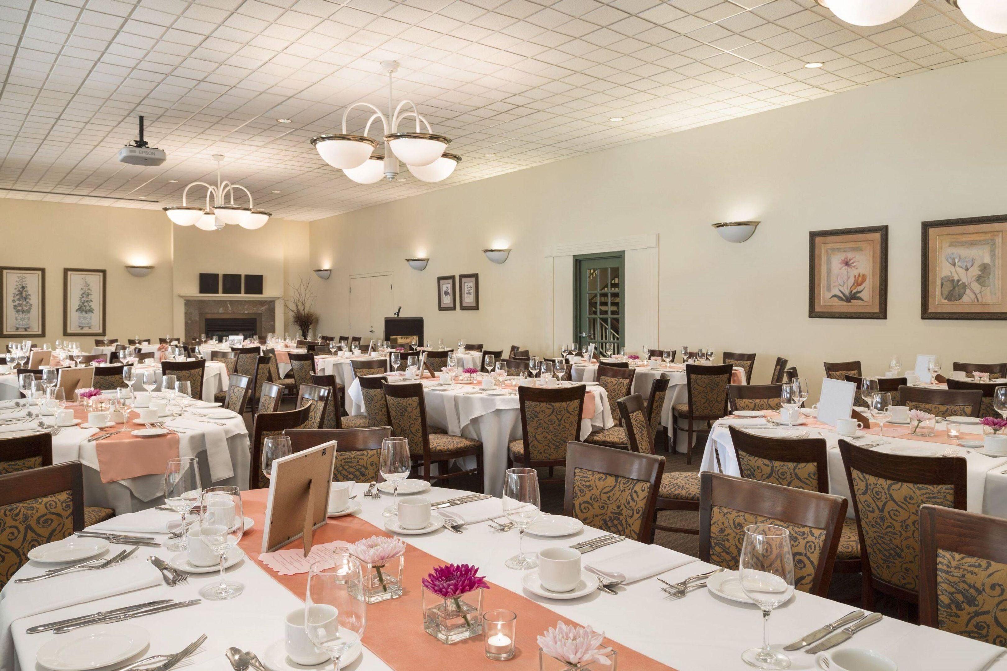 A large dining hall with multiple tables set for service, a fireplace, and wall-mounted light fixtures.