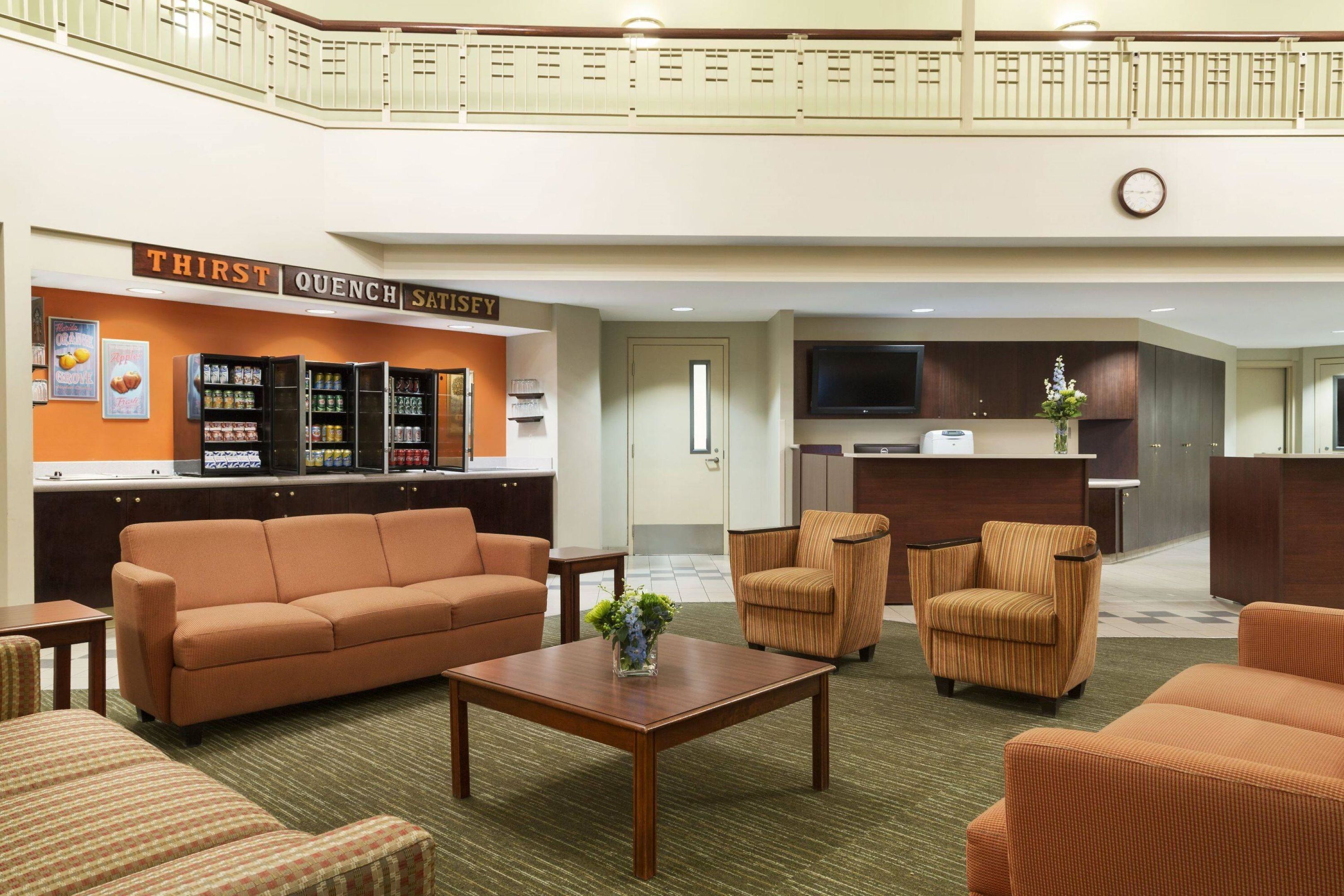 A lobby with a reception desk, a seating area with sofas and armchairs, a vending machine, and a television.