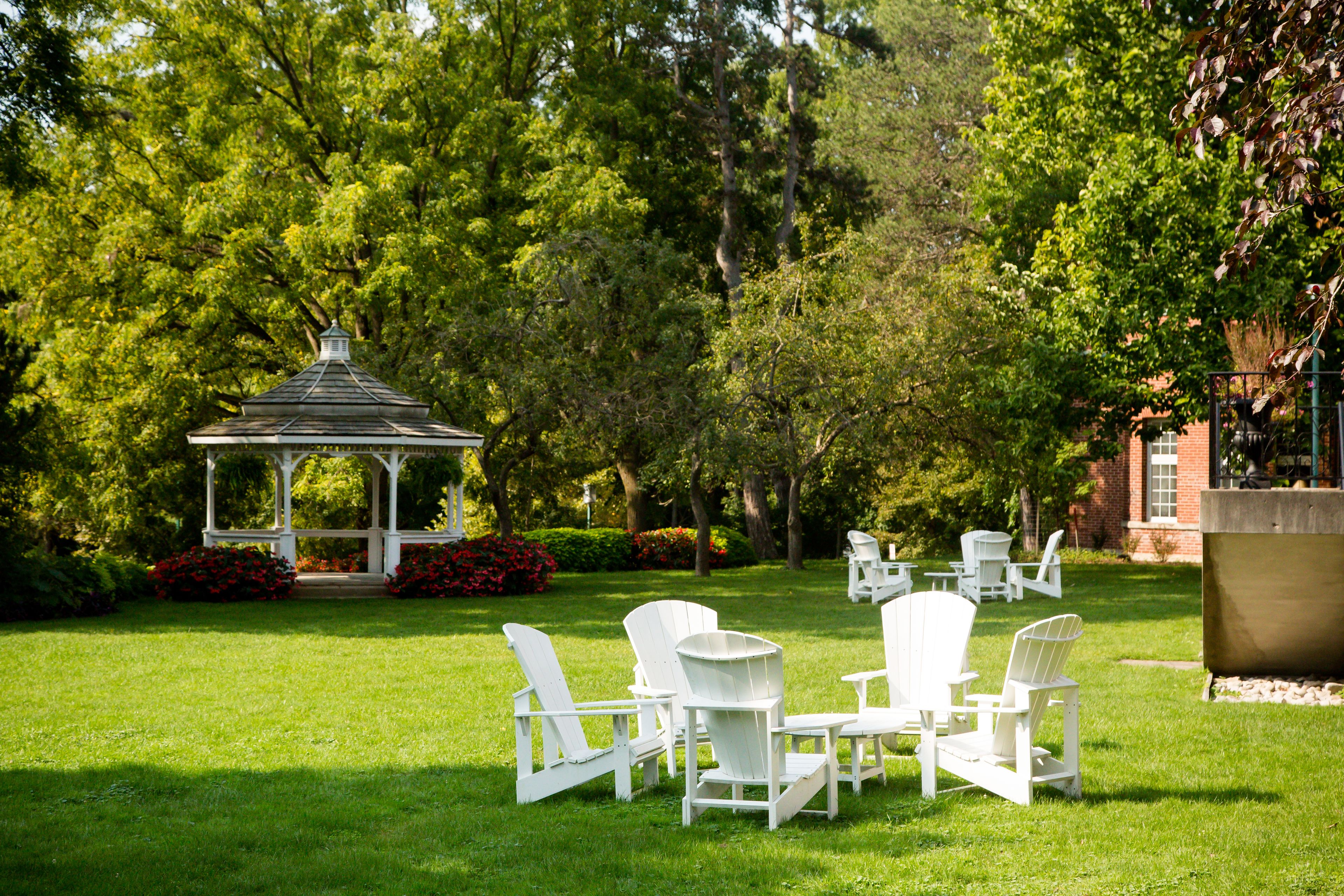 A gazebo surrounded by lush greenery and white outdoor furniture.