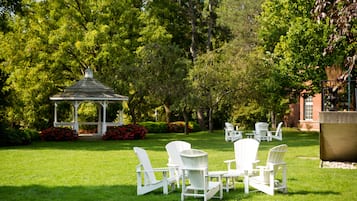 A gazebo surrounded by lush greenery and white outdoor furniture.