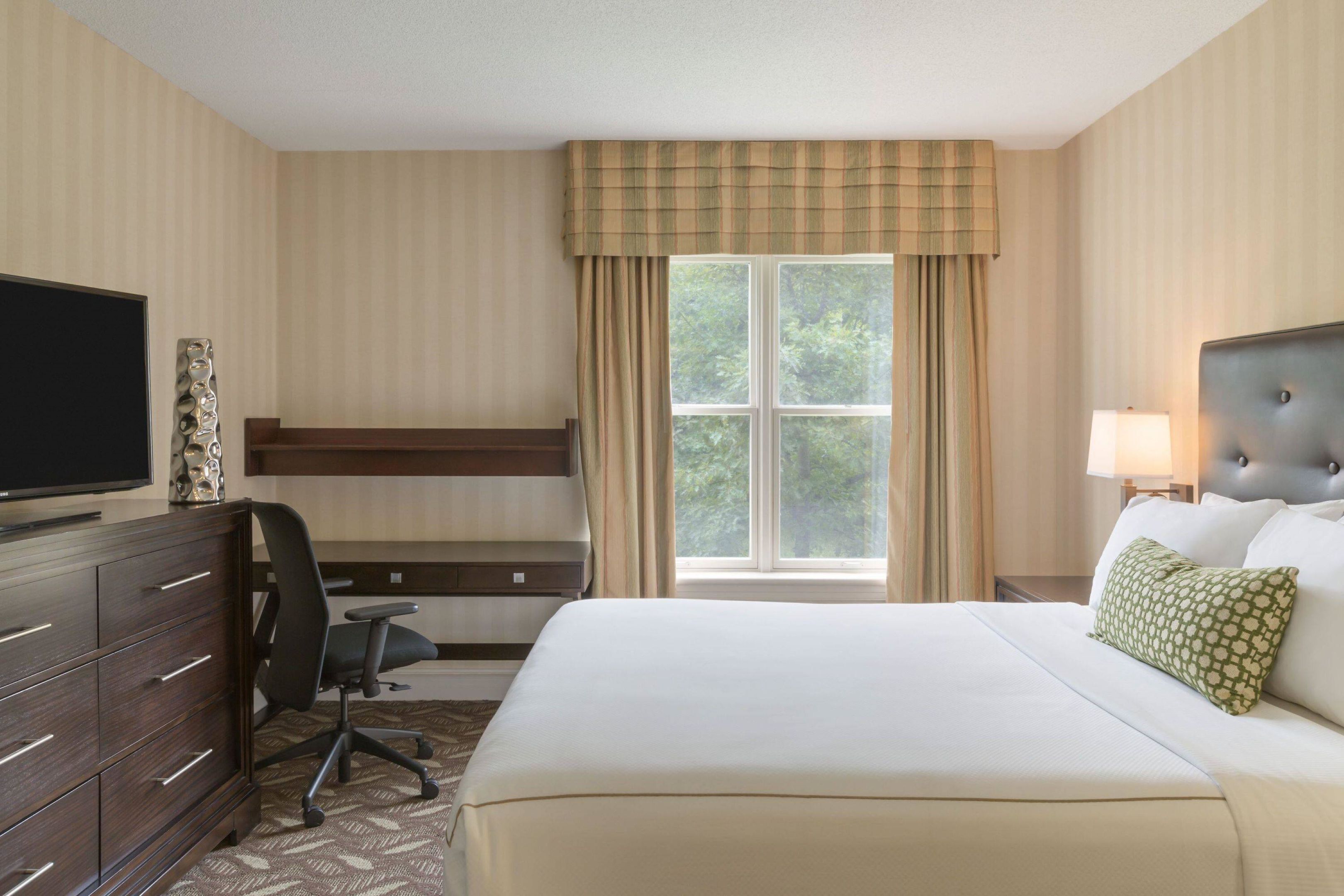 A hotel room with a bed, a desk, a chair, a television, and a window with curtains.