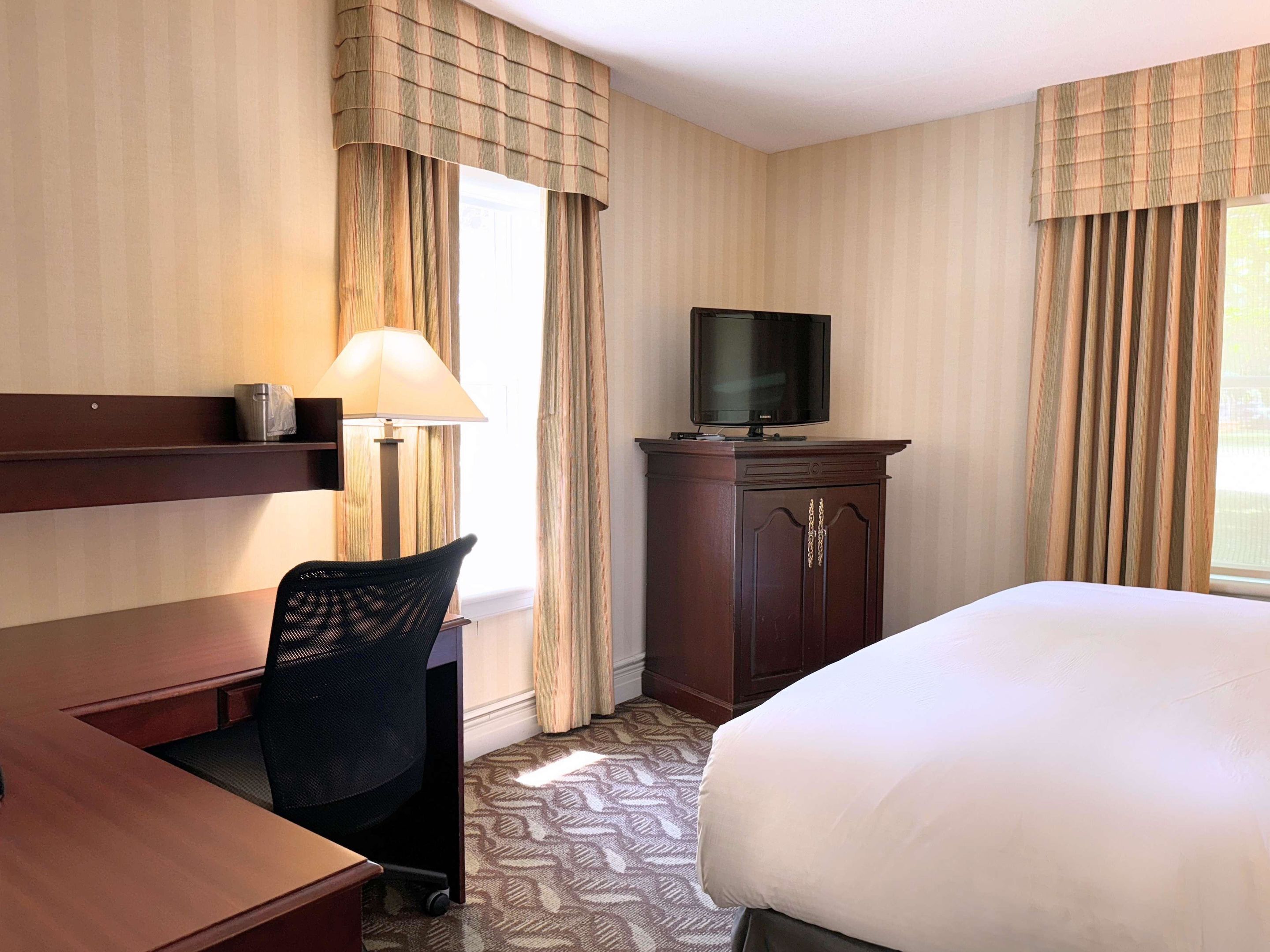 Habitación de hotel con cama, escritorio, silla, televisor sobre un mueble y lámpara.