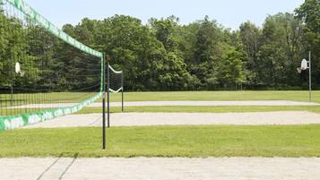 A volleyball court with a net, surrounded by a grassy area and trees.