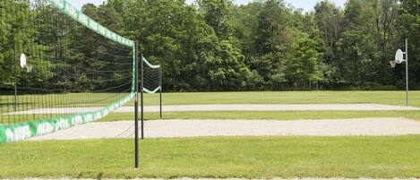 Una cancha de voleibol con red, rodeada de césped y árboles.