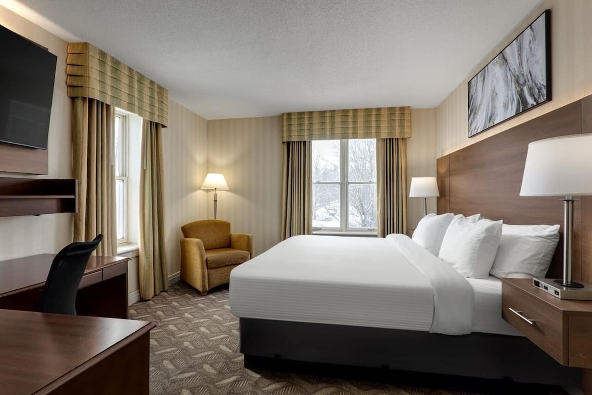 A hotel room with a large bed, a desk, a chair, a TV, and a window with curtains.