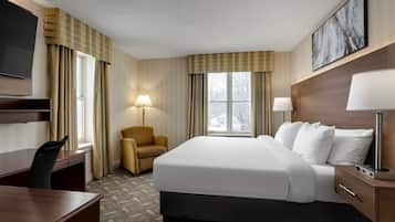 A hotel room with a large bed, a desk, a chair, a TV, and a window with curtains.
