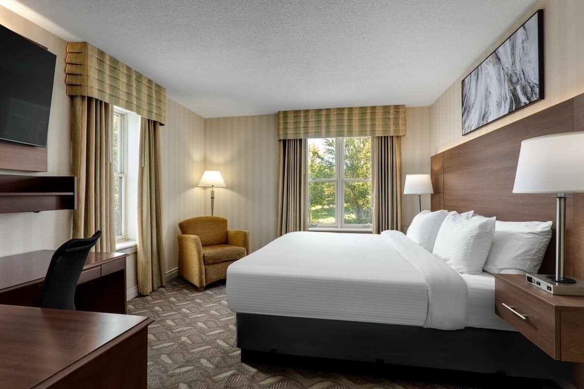 A hotel room with a bed, desk, chair, lamp, and a TV.
