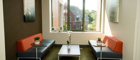 A modern waiting area with two sofas, a small table with a plant, and a large window offering a view of buildings and greenery.