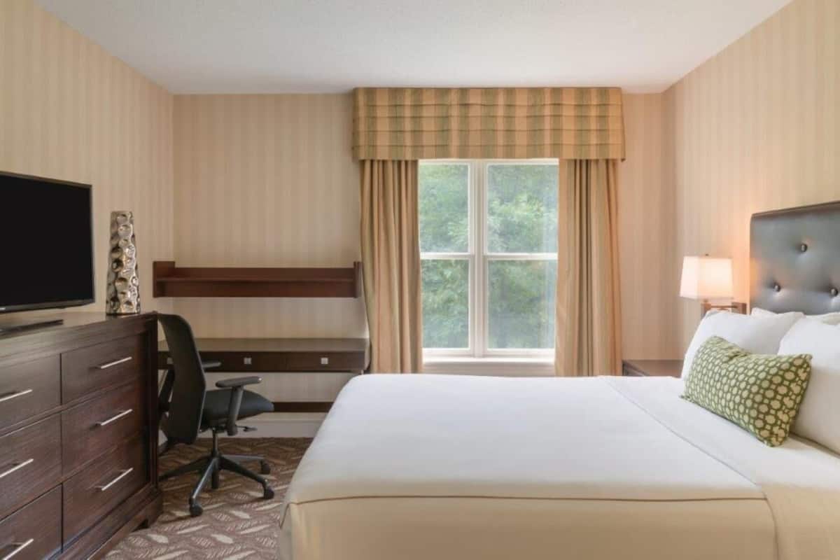 A hotel room with a bed, a desk, a chair, a television, and a window with curtains.