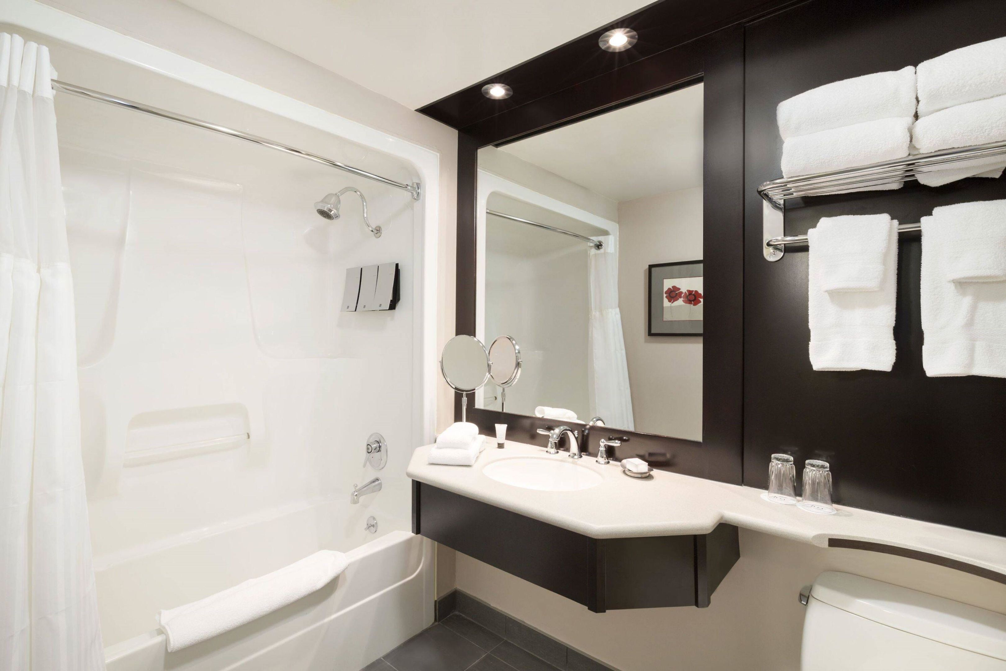 Un baño moderno con bañera, lavamanos, un espejo grande y un perchero para toallas.